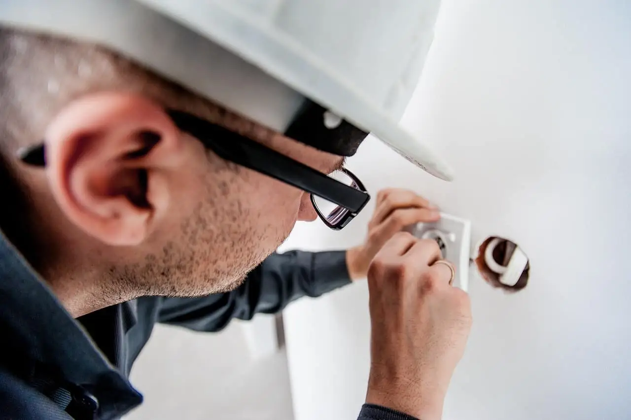 En elektriker med skyddshjälm och glasögon installerar ett eluttag i en vägg.