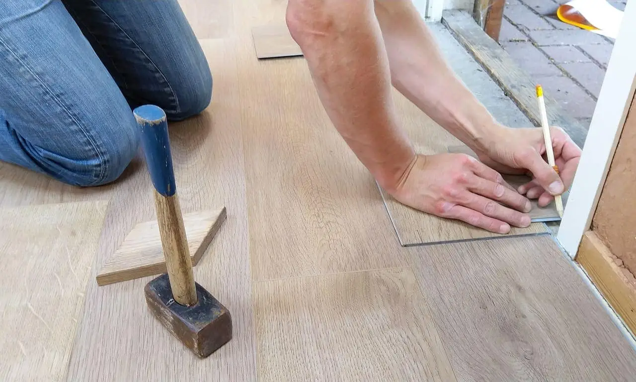 En person i jeans mäter och markerar ett laminatgolv med en penna.
