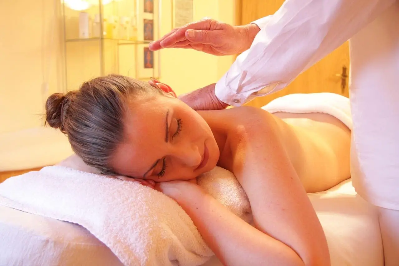 En kvinna ligger på en massagebänk med slutna ögon medan en massör masserar hennes axlar och nacke.